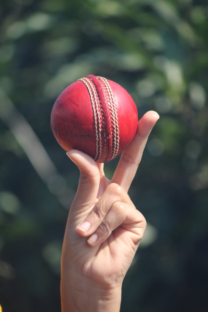 Ipl league 2026 red cricket ball balanced on fingers outdoors in Jabalpur, India.