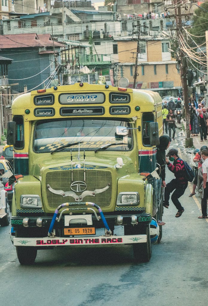 TaTa IPL vibrant commuter bus on a bustling street with people hanging on for a ride.