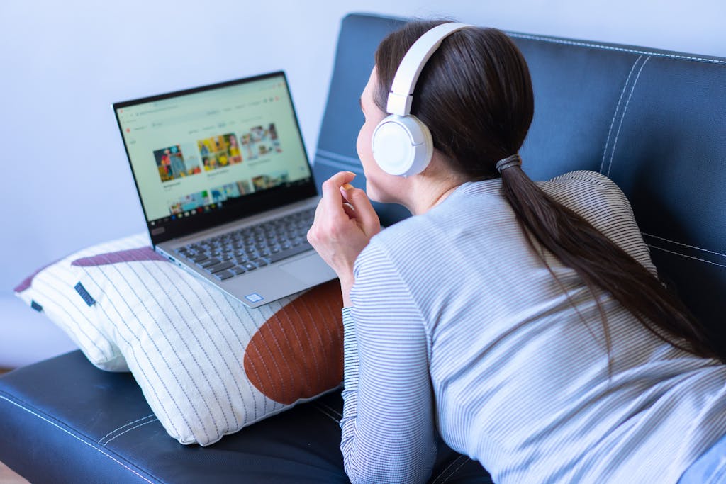 Tata IPL 2026 Live Streaming Free options enjoying leisure time with headphones and a laptop on a sofa.