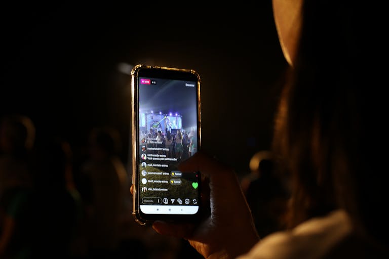 Tata IPL 2026 Live Streaming Free options a concert using her smartphone at night. Vibrant stage in view.