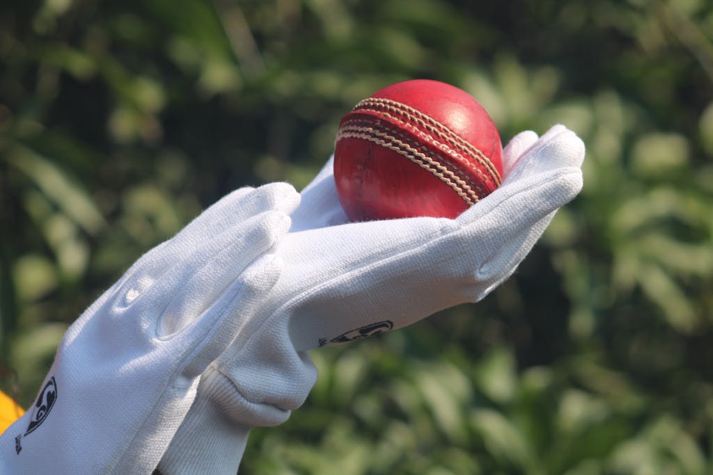 today match prediction of a red cricket ball held by gloved hands outdoors.