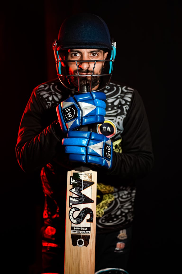 IPL points table prediction cricketer in helmet and gloves holding a cricket bat in a studio setting.