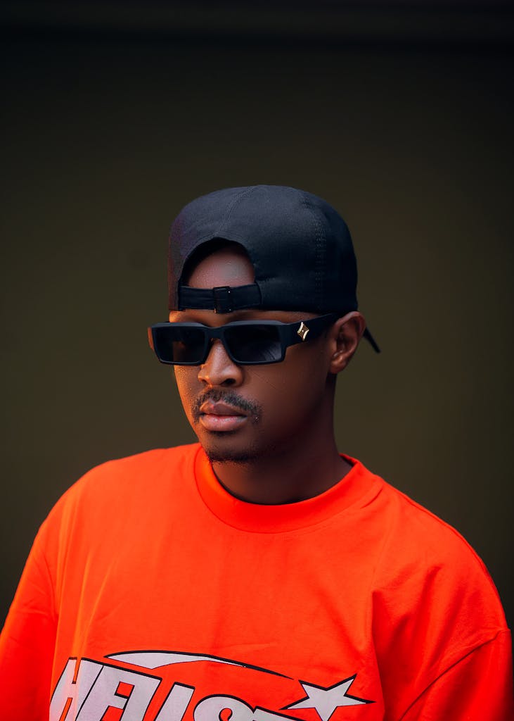 Orange Cap List A fashionable young man wearing sunglasses and an orange t-shirt posing confidently indoors.