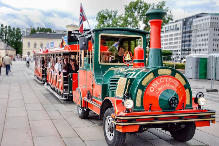circkbuss com A vibrant trackless train touring the streets of Oslo, offering scenic views with passengers enjoying the ride.