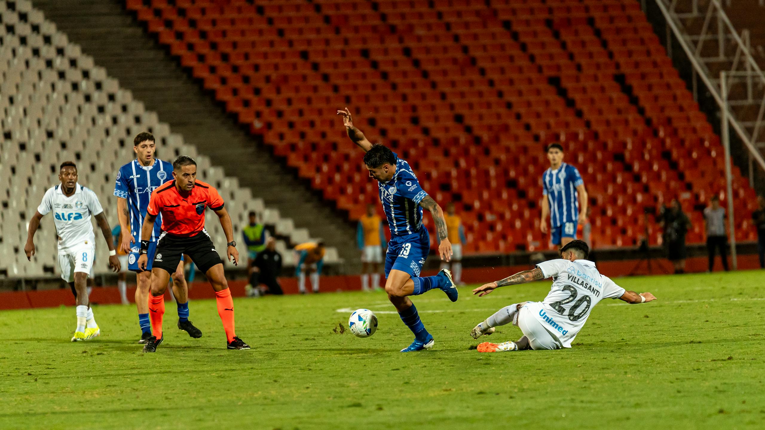 Match Timings IST Dynamic football match with players in action on a green field under stadium lights.