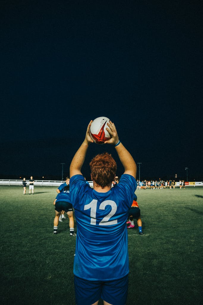 
Match Timings IST Rugby player in blue jersey preparing for lineout during a night game on an outdoor field.